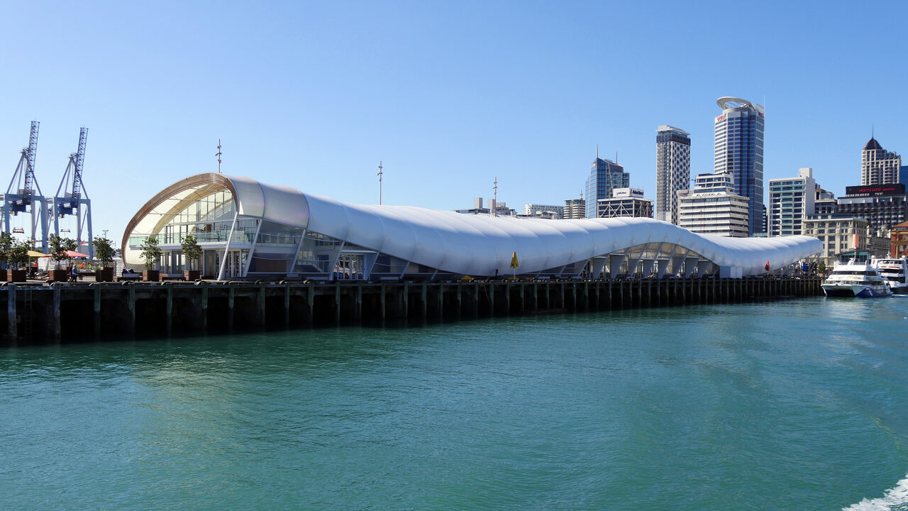 El techo blanco y curvo de la terminal de ferris de Auckland, junto al paseo marítimo, con las torres de la ciudad al fondo