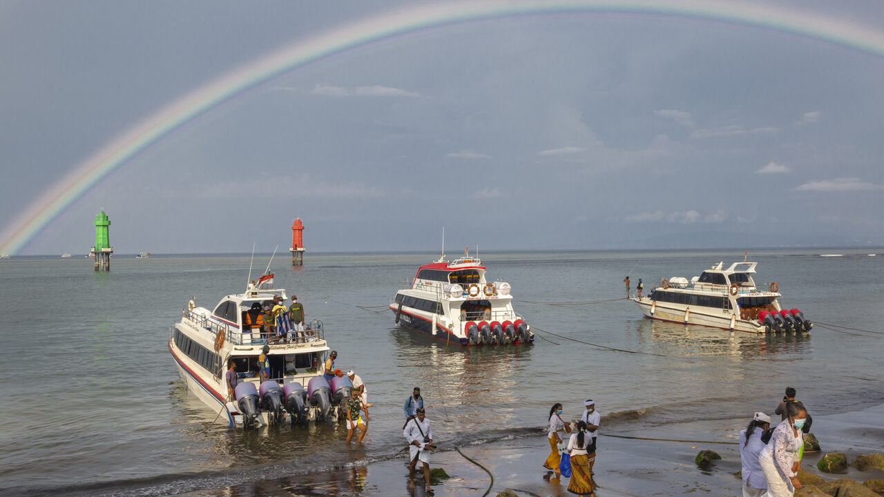 Tres barcos rápidos de pasajeros varados en la orilla del puerto de Sanur bajo un arcoíris