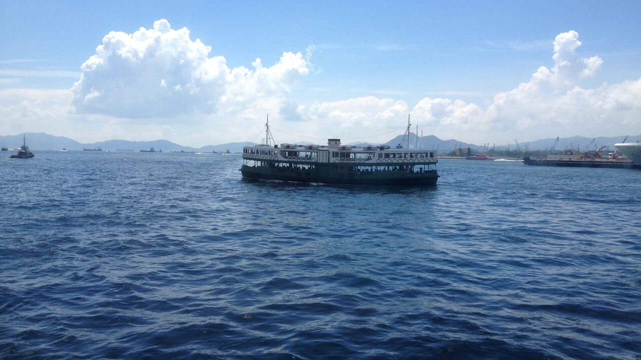 Un Star Ferry verde y blanco cruzando el puerto Victoria bajo un cielo azul, con colinas detrás