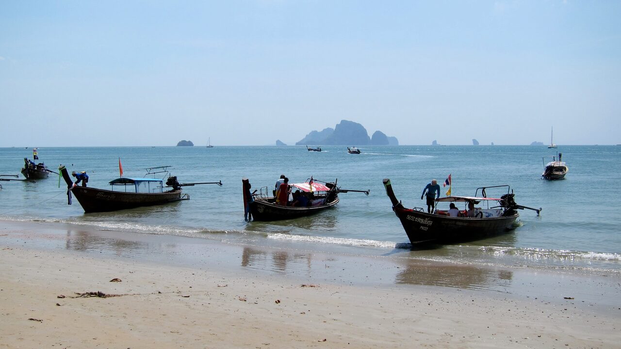 Traditionelle Longtail-Boote auf dem Sand am Strand von Ao Nang, am Horizont Kalksteininseln