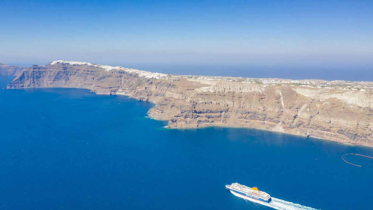 Un barco de Blue Star Ferries saliendo de Santorini, con los acantilados volcánicos y los pueblos blancos de lo alto detrás