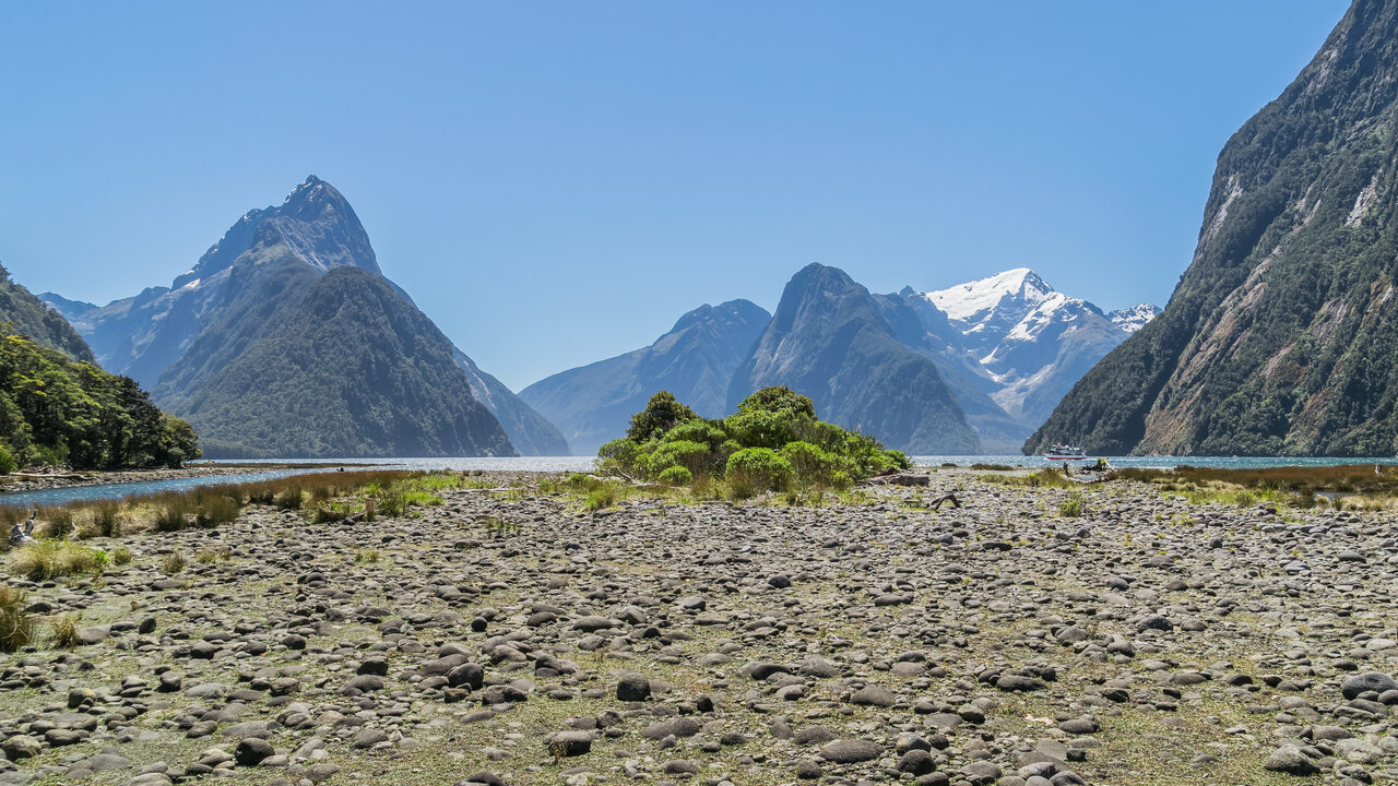 El Mitre Peak y las montañas en la cabecera de Milford Sound, vistos a través de una orilla de guijarros en un día despejado